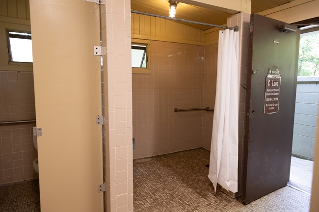the inside of a comfort station has tile flooring and horizontal grab bars in a shower to the right and a bathroom stall to the left