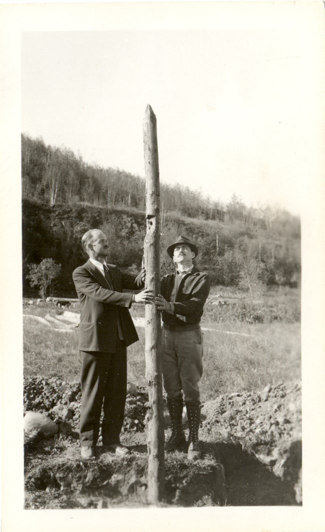 Two men holding a stockade picket twice their height.
