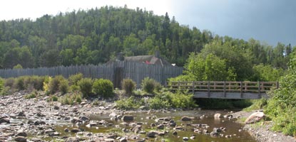 Footbridge across Grand Portage Creek and Great Hall roofline above stockade.