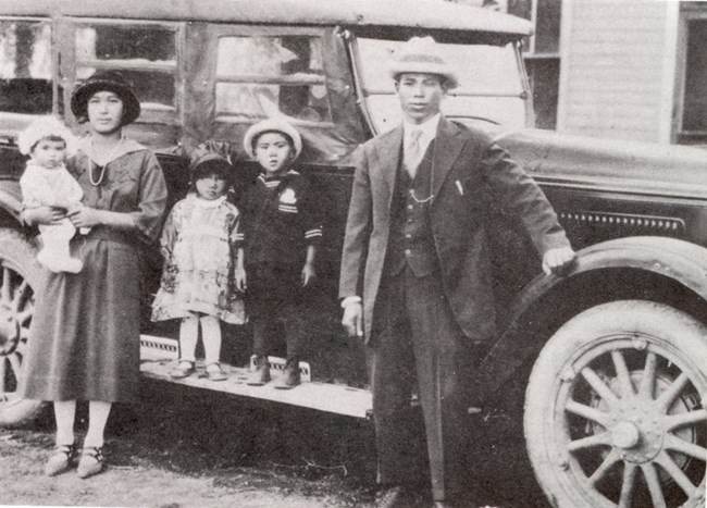 A Japanese American family in fine dress stands beside a vehicle in Alamosa in 1937