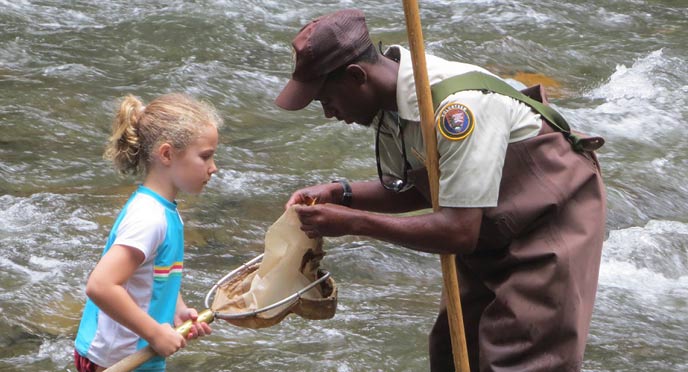 A high school intern netting aquatic invertebrates with a young park visitor