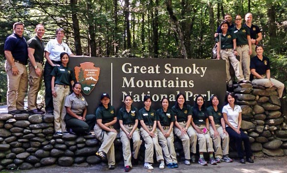 NPS, Cambodian, and Thai park staff pose at the entrance sign to Great Smoky Mountains National Park