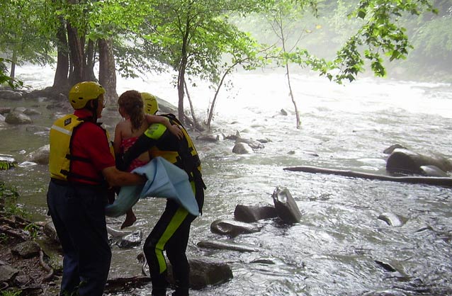 A river rescuer hands a 6-year-old girl to another rescuer waiting on the river bank.