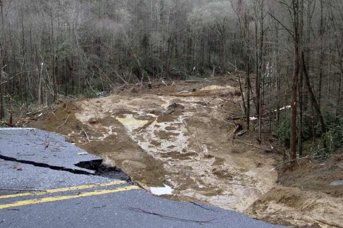 Both lanes of road are washed out with a river of water running where the road used to be