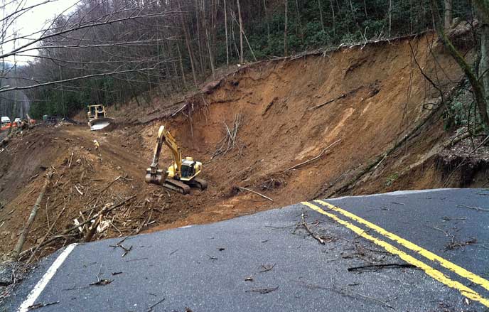 A backhoe working in the landslide area to build an access road to facilitate road repairs.