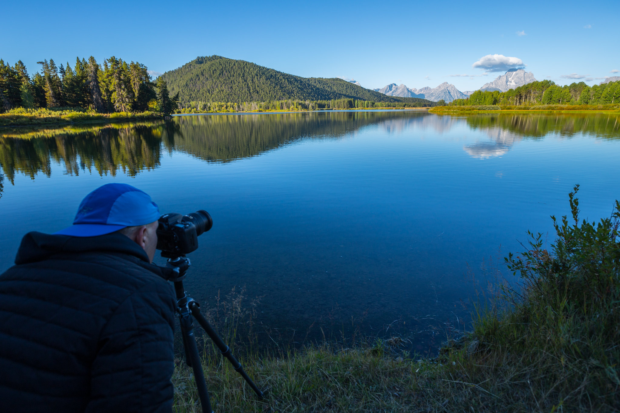 A photographer looks at the Tetons over a lake. 