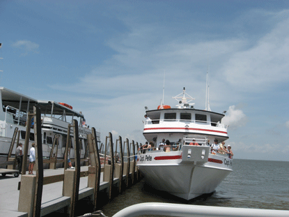 Two white passenger ferries with passengers dock at the West Ship Island pier.  