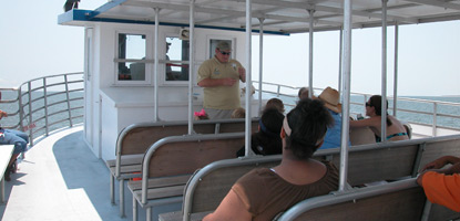 Visitors sit on the top deck of the Ship Island Ferry and listen to a talk on turtles by a transportation interpreter.