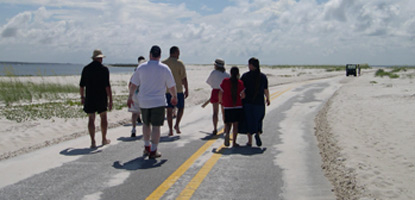 Visitors walk on roadway that has sand covering parts of it.