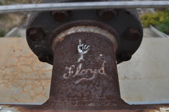 Photo of a signature and a hand, both sculpted from molten welding alloy, pointing to the workmanship of the weld joining a flange to a pipe in the Bravo test area at the Santa Susana Field Laboratory near Canoga Park, California. Photograph, John Wachtel, 2012.
