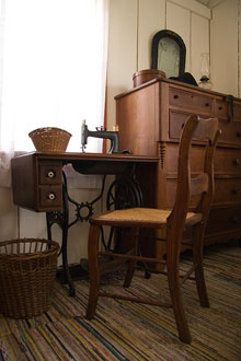 A chair and sewing machine next to a dresser and a window.