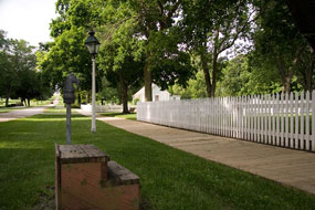 Wooden boardwalks and white picket fences line a historic street.