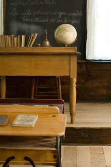 A historic classroom's teacher's desk and blackboard as seen from the pupils' desk.