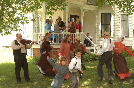 Living history volunteers in 19th century dress dancing to a fiddler.