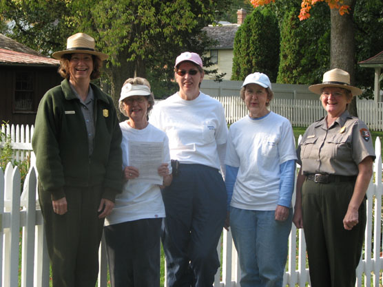 Two women in National Park Ranger uniforms and three women in white Hawkeye Hiker tee-shirts pose by a picket fence.