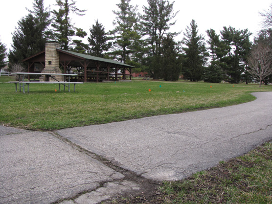 A cracked and buckled asphalt walkway leads past a picnic shelter.