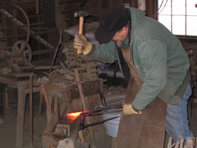A blacksmith wearing gloves and a leather apron hammers hot metal on an anvil.