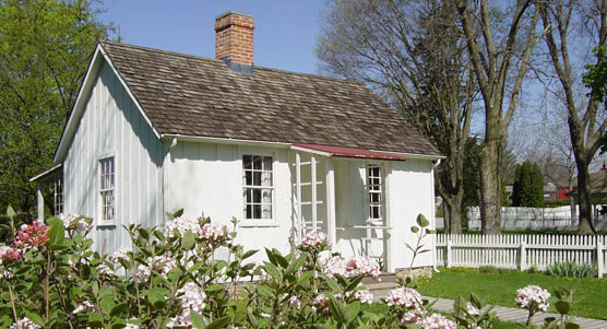 A small white cottage with pink-flowering bushes in the foreground.