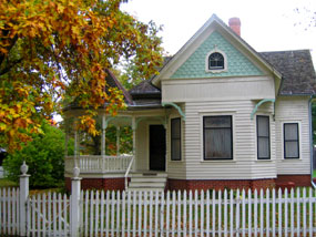 Leaves in fall foliage over the porch of a white house with blue trim.