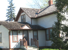 A cream colored one and a half story house with brown trim.