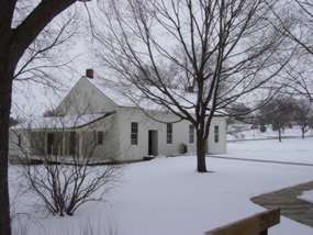 White frame Friends Meetinghouse and leafless trees in the snow.