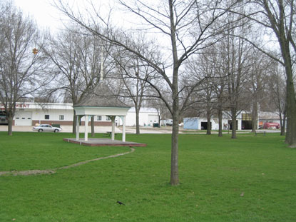 A grassy lawn with a small bandstand and trees.