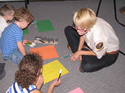A woman helps pre-school children write poems with markers and construction paper.