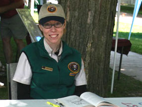 A woman in a volunteer uniform seated at an outdoor table.