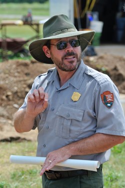 A man wearing a green hat and dark sunglasses speaking to an unseen person