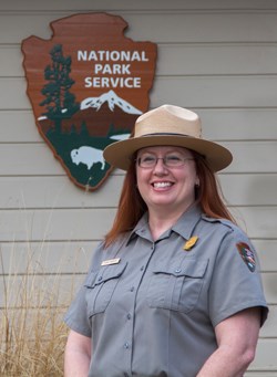 A ranger wearing a flat hat and standing in front of the NPS arrowhead