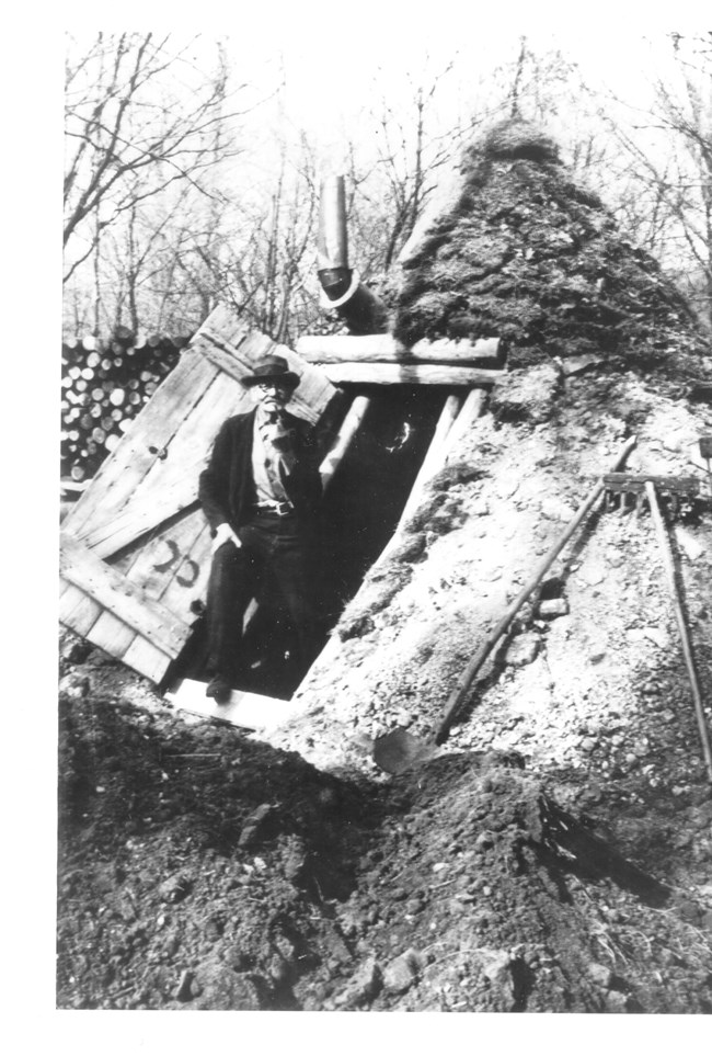 Man stands in earthen hut.