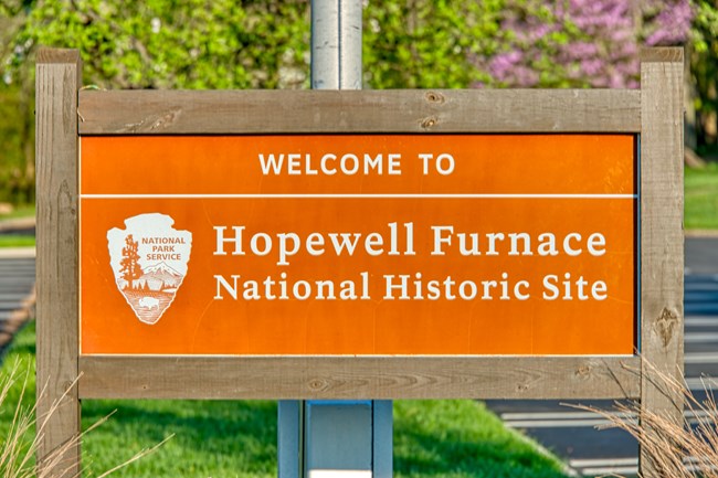 Brown sign with NPS arrowhead that reads "Welcome to Hopewell Furnace National Historic Site".