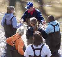 Volunteer helps students collect samples from Cub Creek.