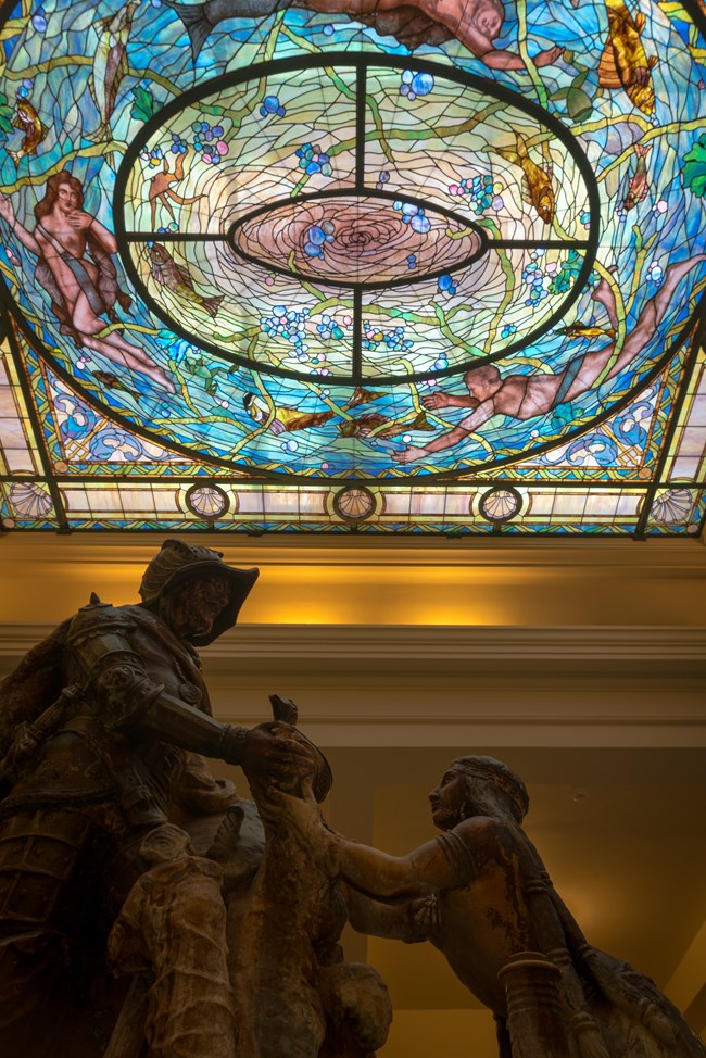 Statue of early explore and Native American woman under a stained glass ceiling