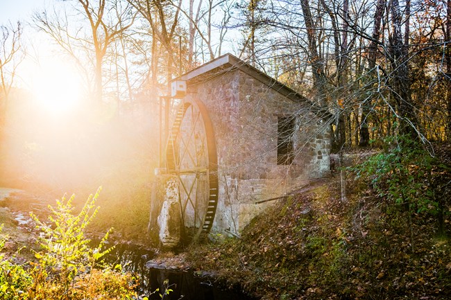 Water wheelhouse with sun setting through forest