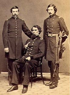 sepia tone image of three men in Union Army uniforms. One is seated with the other two flanking. All have dark hair.