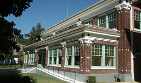 color photo of the Superior Bathhouse from the south end. It is a two-story dark red brick with many windows and the windows have a lime green trim.