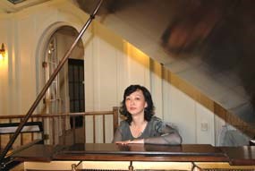 Asian woman sitting at piano, shot from across piano with lid up