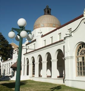 Photo of Quapaw Bathhouse from south end, showing front of building. Building is white stucco, Spanish revival style architecture and has a large mosaic dome in center of building