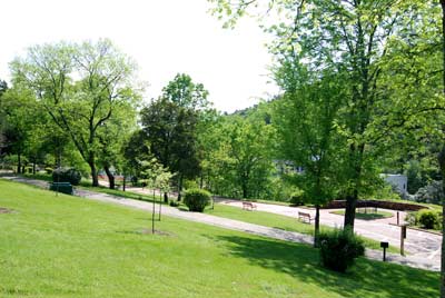 Grassy hillside on left, below on right is a paved trail and a bricked walkway with a number of trees.