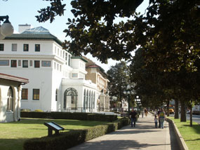 Portion of Bathhouse Row, with Maurice Bathhouse on left, magnolia trees on right and visitors on the wide sidewalk.