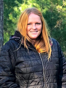 Robin wearing a black jacket in a forested area