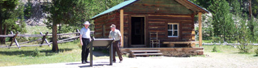 a photo of a visitor reading a sign in front of the Joe Fleshut cabin, in the Kawuneeche Valley