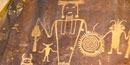 Picture of anthropomorphic figure holding a circular shape pecked into a rock.