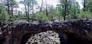 A hiker stands on a lava bridge in Big Tubes