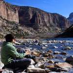 A hiker rests along the Green River at the end of the Jones Hole Trail
