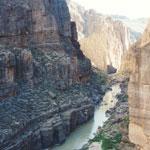 Far below rock walls, the river runs smoothly through patchs of sun and shadow