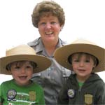 Two new Junior Rangers show off their badges while our ranger lends some real ranger hats to try on!
