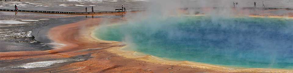 Visitors stand on the boardwalk of Grand Prismatic, the park's largest hot spring which is ringed with orange, brown and yellow runoff channels.