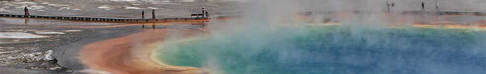 Visitors stand on the boardwalk of Grand Prismatic, the park's largest hot spring which is ringed with orange, brown and yellow runoff channels.